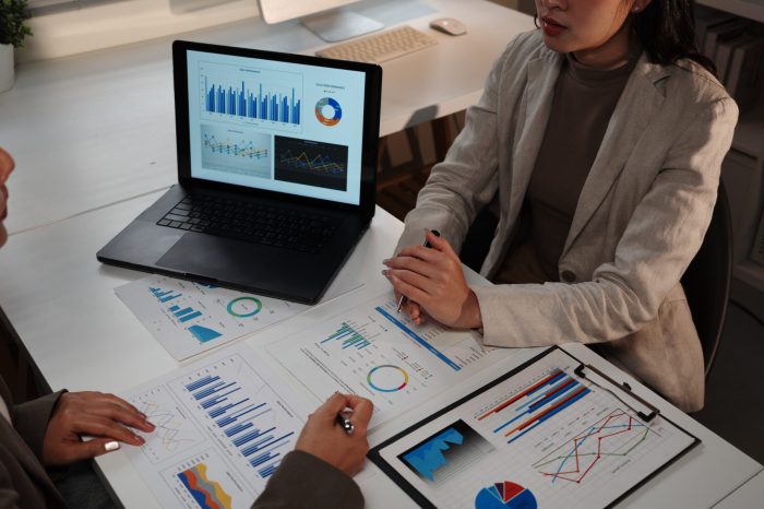 Business team working with data analyzing charts and graphs discussing project strategy using laptop at night in office